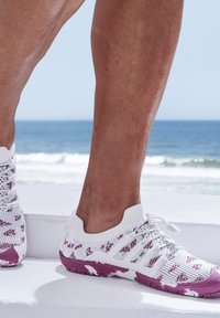 Weiße Sportschuhe mit einem strukturierten Strickobermaterial, das burgunderfarbene Akzente und einen sockenähnlichen Kragen aufweist, kombiniert mit einer lila Gummisohle.