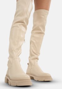 Botas de cuero beige hasta la rodilla con un diseño holgado, punta redondeada y suela de plataforma gruesa. Cremalleras laterales para facilitar el uso.