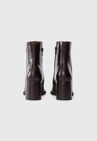 Bottines en cuir marron avec un talon chunky et une fermeture éclair sur le côté, présentant une texture lisse et de subtils détails de couture.