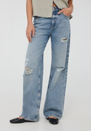 Jeans azzurri chiari a vita alta, a gamba larga, con toppe strappate e orli sfilacciati. Realizzati in denim con una consistenza morbida e una vestibilità comoda.