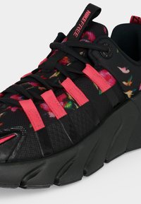 Μαύρο αθλητικό παπούτσι Nike Free με παχιά σόλα, ροζ λεπτομέρειες, μοτίβα λουλουδιών και πουλιών και μαύρα κορδόνια που διασταυρώνονται με ροζ βρόχους.