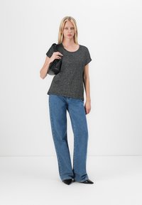 Gray short-sleeve top, loose fit, paired with high-waisted, wide-leg blue jeans. Model holds a small black handbag. Simple and casual design.