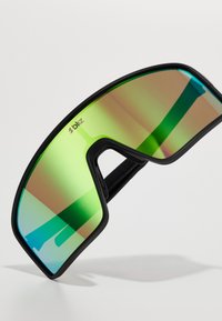 Lunettes de soleil avec une monture noire, de grandes verres teintés de vert avec un effet dégradé, et un design enveloppant pour un look moderne.