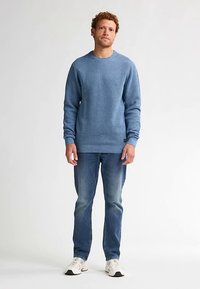 Pulover albastru din tricot cu model nervurat, gât rotund, purtat peste blugi bleu deschis și teniși albi. Are mâneci lungi și croială dreaptă.