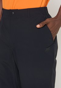 Czarne spodnie o gładkim wykończeniu tekstylnym, z bocznymi kieszeniami i subtelnym logo na udzie, zaprojektowane z myślą o komforcie i swobodzie ruchów.