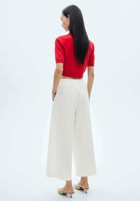 Rood cropped gebreid top, brede crèmekleurige broek, gladde textuur, elastische tailleband en beige hakken, gezien vanuit de achterkant.