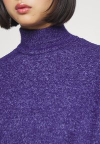 Lila polokrage tröja i mjukt och strukturerat tyg, med ribbat halsband och ett subtilt marmorerat mönster över hela ytan.