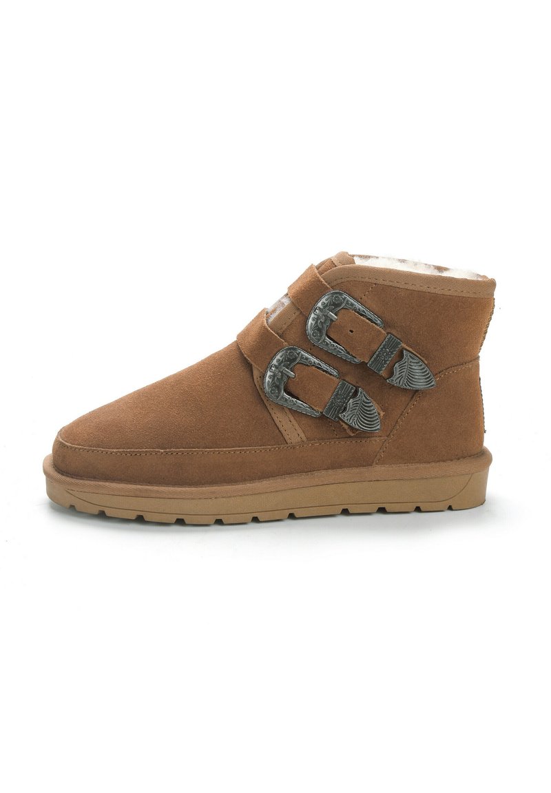 Botas de tobillo de ante marrón con dos hebillas plateadas, forro de pelaje sintético, punta redonda y suela de goma. Diseñadas con una forma de media caña.