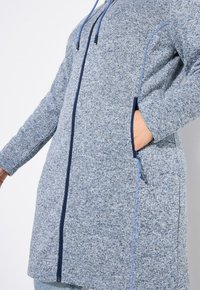 Blått heather-färgat långt cardigan med dragkedja fram, blå snörning i huvan och sidofickor med kontrasterande marinblå detaljer.