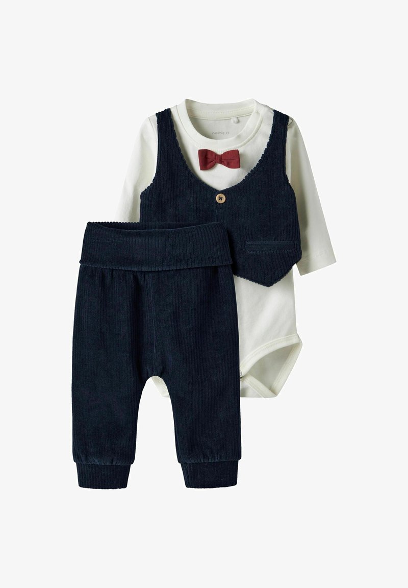 Chaleco de pana azul oscuro con botones, bodysuit de manga larga blanco y pantalones a juego con cintura y puños acanalados. Acento de pajarita roja.