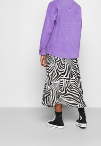 Purple corduroy shirt, black and white zebra-print midi skirt, and black high-top sneakers. Features button details and a relaxed fit.
