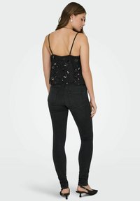 Czarny krótki top na cienkich ramiączkach z cekinami, połączony z dopasowanymi czarnymi jeansami. Prezentuje teksturowany wzór i styl bez pleców.
