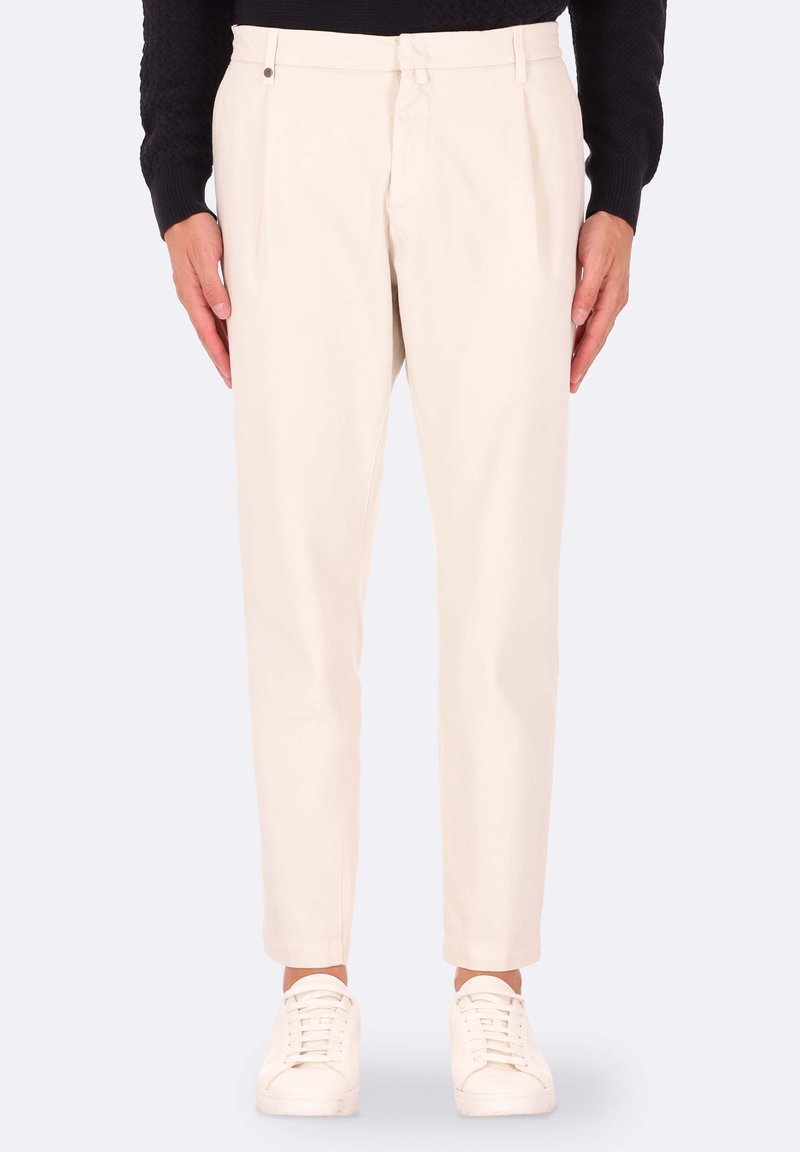 Pantaloni beige a sigaretta realizzati in un tessuto liscio, con pieghe frontali e una vita standard, abbinati a sneaker bianche.