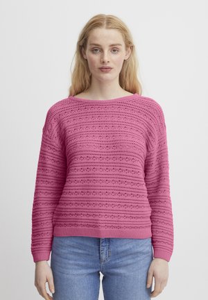 Maglione rosa lavorato a maglia con motivi a strisce orizzontali, collo rotondo e maniche lunghe, abbinato a jeans azzurri chiari. Texture morbida.