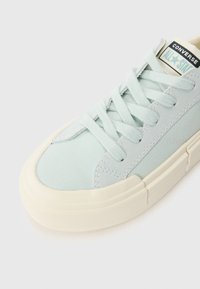 Baskets Converse All Star bleu clair avec semelle et lacets en caoutchouc blanc, montrant les détails des orteils et du côté sur un fond uni.