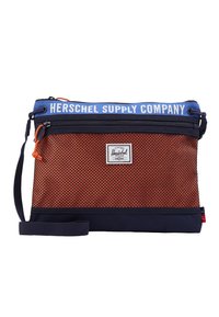 Oranžová síťovaná taška s námořnickým dnem a popruhem, se modrou vrchní částí s textem "HERSCHEL SUPPLY COMPANY" a malou nášivkou s logem.
