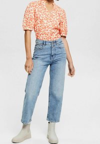 Orangenbluse mit Blumenmuster und kurzen Puffärmeln, kombiniert mit hellblauen, hochgeschnittenen Jeans und grauen Stiefeletten mit gerippten Sohlen.