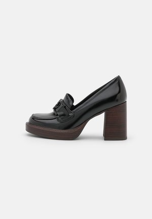 Mocassin en cuir verni noir avec talon épais en bois superposé et boucle décorative sur le dessus, présenté de profil sur fond blanc.