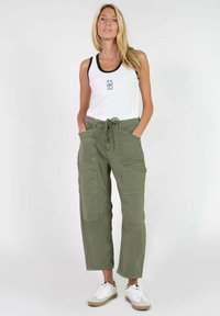 Pantalones cargo verde oliva con múltiples bolsillos, cintura con cordón y un corte relajado, combinados con una camiseta sin mangas blanca con detalles en azul marino.