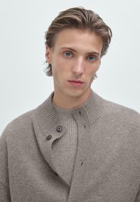 Jasnobrązowy sweter z dzianiny z prążkowanym kołnierzem i zapięciami na guziki. Gładka tekstura, dopasowany krój i subtelne tonalne wariacje.