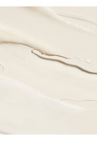 Liquide beige lisse et crémeux étalé uniformément avec des stries visibles et un léger éclat, suggérant texture et épaisseur.