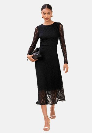 Must pitskleit pikkade varrukatega ja keha järgiva ülaosaga, sirge lõike ja põlve alt ulatuva pikkusega. Kaunistatud väikese käekotiga.