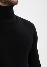 Pull noir à col roulé, fabriqué en matériau doux, présentant un design ajusté avec un col côtelé et une texture lisse.