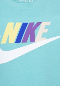 Lyseblå Nike T-skjorte med fet, flerfarget "NIKE"-tekst i gul, blå, lilla og beige, med en hvit swoosh-design.