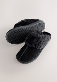 Chaussons en daim noir avec un poignet en fausse fourrure gris foncé et moelleuse. La semelle extérieure présente une texture striée pour l'adhérence. Design simple à enfiler.