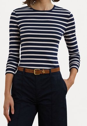 Mujer con camisa de manga larga a rayas en azul marino y blanco, pantalones oscuros de talle alto y cinturón de cuero marrón con hebilla dorada e iniciales RLL.