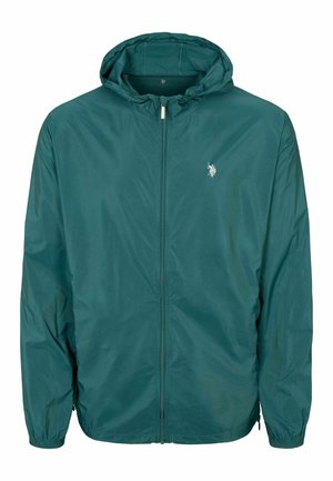 Tirkīza krāsas vēja jacķis ar kapuci, pilnu rāvējslēdzēju, elastīgiem piedurknēm un mazu logo uz krūtīm. Viegls, gluds tekstūra un ikdienišķs dizains.