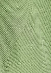 Gros plan d’un tissu tricoté côtelé vert clair montrant des motifs de côtes diagonales et verticales et une texture douce.