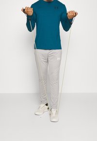 Teal pitkähihaine urheilupaita, vaaleanharmaat kapenevat housut ja valkoiset lenkkarit. Pitelee vastuskuminauhoja, joissa on minimaliset muotoiluyksityiskohdat.