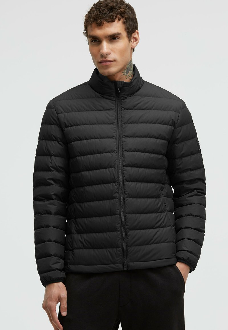 Black padded jacket with a high collar, featuring horizontal quilted seams, zip closure, and side pockets. Smooth, lightweight fabric.