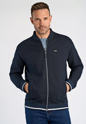 Chaqueta de cremallera azul marino hecha de material suave; presenta puños y dobladillo acanalados con rayas en azul claro y blanco; incluye un pequeño acento de logo.