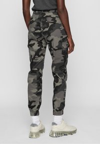 Maskuotos kelnės cargo stiliaus pilkų ir juodų atspalvių, su elastingomis rankogaliais, daugybe kišenių ir laisvo kirpimo. Derinamos su lengvais sportbačiais.