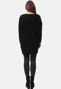 Schwarzer, gestrickter Oversized-Pullover mit weitem Ausschnitt und langen Ärmeln. Er hat ein strukturiertes Muster und eine lockere Passform und wird mit grauen Skinny-Jeans kombiniert.