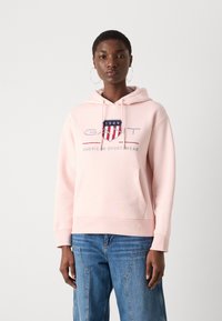 Roze hoodie met een voorzak, capuchon met trekkoord en GANT-logo met blauwe en rode accenten. Zachte stof en een relaxte pasvorm.