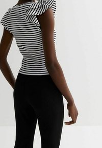 Černobílý pruhovaný top s volánkovými rukávy, přiléhavý design a žebrovaná textura. V kombinaci s černými kalhotami, které zvýrazňují elegantní siluetu.