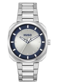 Reloj de acero inoxidable plateado con un bisel azul oscuro, esfera plateada, marcadores de hora blancos y una pulsera de eslabones de metal. Presenta un diseño simple y moderno.