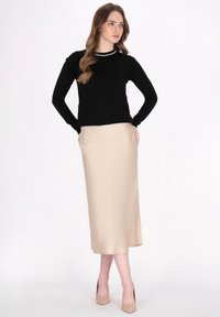 Maglione lungo nero a maniche lunghe con dettaglio colletto bianco abbinato a una gonna midi satin beige. Le caratteristiche principali includono una silhouette aderente e una texture liscia.