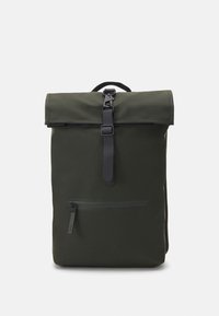 Un sac à dos vert foncé en tissu résistant, doté d'un design à rabat, d'une fermeture à boucle noire et d'une poche zippée à l'avant.