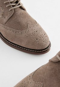 Bruine suède brogue schoenen met een puntige neus, decoratieve perforaties en contrasterende stiksels langs de zool.