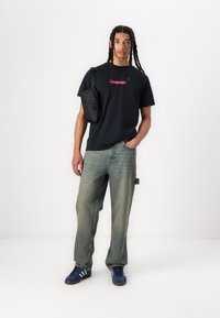 Black t-shirt with pink logo, loose blue jeans, and blue sneakers with white stripes. Black crossbody bag, straight shape, casual style.