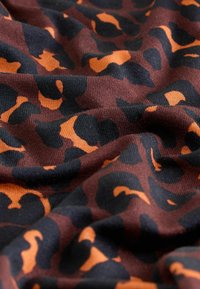 Brūns audums ar drosmīgu melnas un oranžas leoparda raksta rakstu, kas demonstrē mīkstu, teksturētu virsmu ar nelielu elastību.