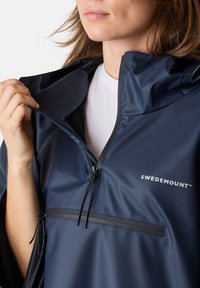 Navyblå regnponcho med halvmatchad krage, justerbara snoddar och en ficka fram, tillverkad av slätt, vattentätt material.