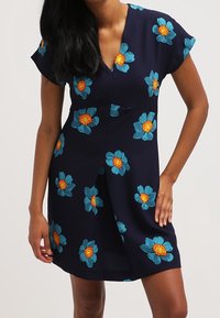 Vestido de marina con estampado floral, que presenta grandes flores azules y centros amarillos. Mangas cortas y diseño de escote en v. Tela suave.