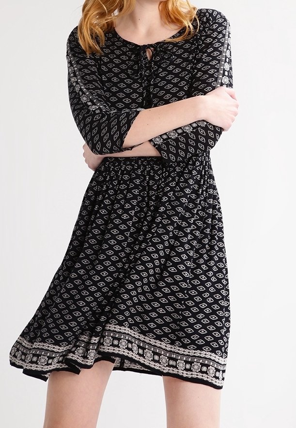 Vestido negro con mangas de tres cuartos, que presenta un patrón de diamantes, cintura ajustada y un dobladillo decorativo. Tejido texturizado con un corte holgado.