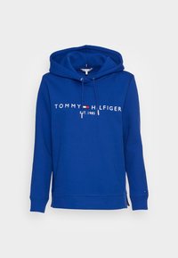 Felpa blu con cappuccio e cordino, con logo "TOMMY HILFIGER" e testo "Est. 1985" in bianco. Tessuto morbido, maniche lunghe, polsini a costine, spacchi laterali.