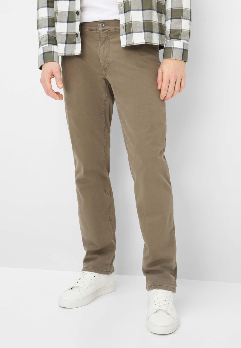 Hellbraune Chino-Hosen aus Baumwolle mit schmaler Passform, ausgestattet mit vorderen Taschen und einem Reißverschluss, kombiniert mit weißen Turnschuhen und einem karierten Hemd.